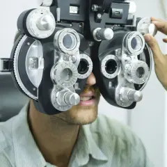 Badanie wzroku. Nie noszenie okularów skutki mogą być poważne. Optometrysta reguluje refraktorem.