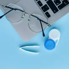 Okulary, pojemnik na soczewki i pęseta na laptopie. Czy można nosić soczewki i okulary jednocześnie? Tak, jeśli potrzebujesz korekcji wzroku.