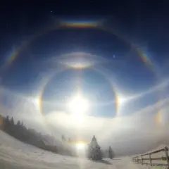 Niesamowity efekt halo oczu na zimowym niebie, otaczający słońce wieloma tęczowymi kręgami.