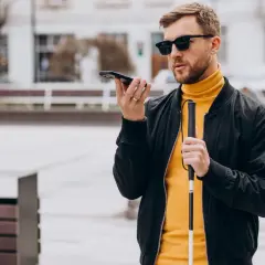 Mężczyzna w okularach, trzymający laskę i telefon, korzysta z technologii, która może być pomocna jak okulary dla niewidomych.