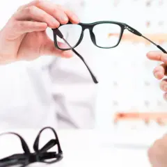 Dopłata do okularów: optyk prezentuje nowe okulary, w tle leżą kolejne.