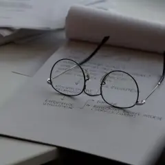 Okulary leżą na notatniku z planami. Czas na wymianę szkieł w okularach, by lepiej widzieć cele projektu.