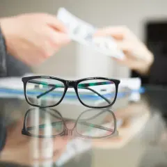 Okulary na pierwszym planie, w tle ręce przekazujące pieniądze. Czy optyk zrobi okulary bez recepty?