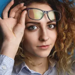 Kobieta z burzą rudych loków poprawia okulary. Zastanawia się, jakie fotochromy wybrać, by pasowały do jej stylu.