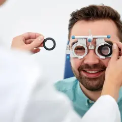Optometrysta bada wzrok mężczyzny, który uśmiecha się, nosząc specjalne okulary.