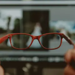 Czerwone okulary na tle monitora z rozmazanymi zdjęciami. Dobre widzenie obuoczne pozwala dostrzec detale.