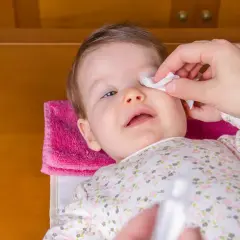Delikatne przemywanie oczu niemowlaka wacikiem. Rodzic dba o higienę maluszka, pokazując, czym przemywać oczy.