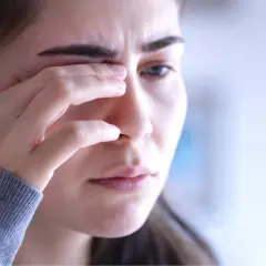 Kobieta z zaciśniętymi powiekami, być może zmagająca się z zaćmą pourazową.