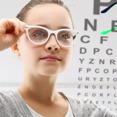 Dziewczynka z okularami na tle tablicy Snellena. Czy -1.25 to duża wada wzroku?