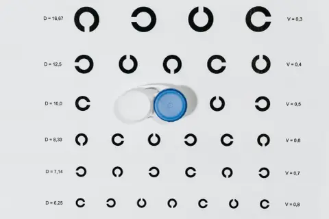 Na tablicy optometrycznej widać szereg symboli "C" oraz pojemnik na soczewki. Wartości D i V sugerują dobór soczewek, np. krzywizna soczewki 8,6 i 8,7.