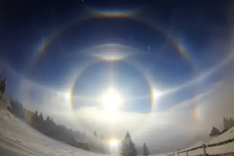 Niesamowity efekt halo oczu na zimowym niebie, otaczający słońce wieloma tęczowymi kręgami.
