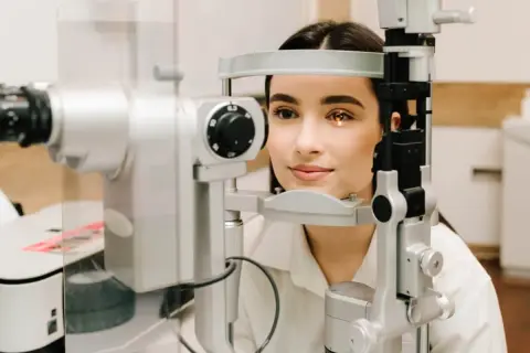 Młoda kobieta podczas badania dna oka. Przygotowanie do wizyty u okulisty, światło lampy oświetla jej oko.