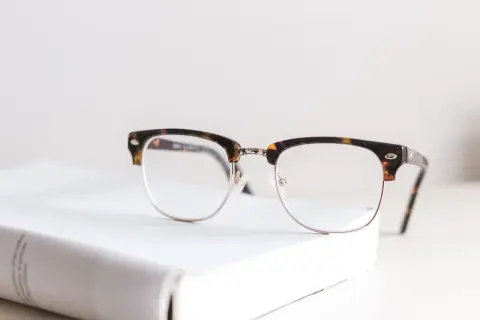 Okulary w stylu retro na białej książce. Nawet najmniejsza wada wzroku może wymagać takiego wsparcia.