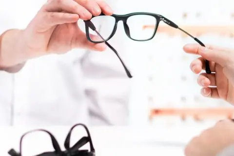 Dopłata do okularów: optyk prezentuje nowe okulary, w tle leżą kolejne.