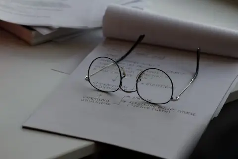 Okulary leżą na notatniku z planami. Czas na wymianę szkieł w okularach, by lepiej widzieć cele projektu.