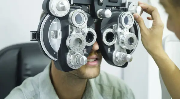 Badanie wzroku. Nie noszenie okularów skutki mogą być poważne. Optometrysta reguluje refraktorem.