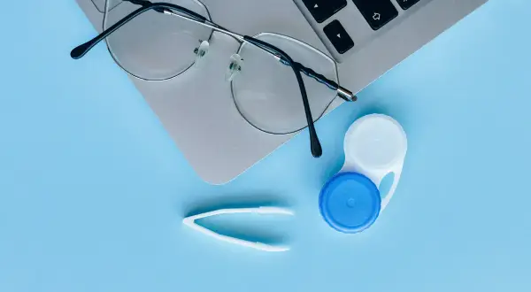 Okulary, pojemnik na soczewki i pęseta na laptopie. Czy można nosić soczewki i okulary jednocześnie? Tak, jeśli potrzebujesz korekcji wzroku.