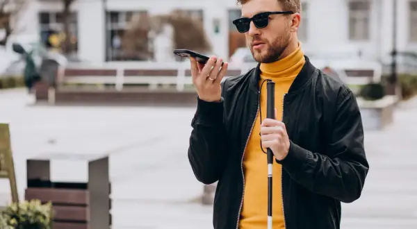 Mężczyzna w okularach, trzymający laskę i telefon, korzysta z technologii, która może być pomocna jak okulary dla niewidomych.
