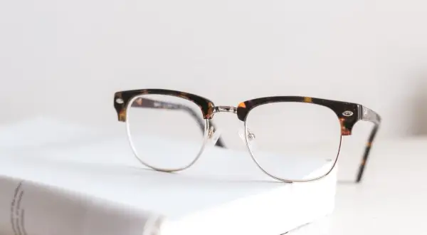 Okulary w stylu retro na białej książce. Nawet najmniejsza wada wzroku może wymagać takiego wsparcia.