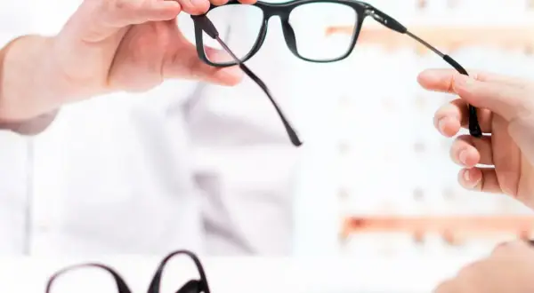 Dopłata do okularów: optyk prezentuje nowe okulary, w tle leżą kolejne.