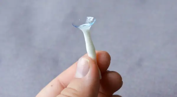 Dłoń trzyma aplikator z jedną zdrową soczewką kontaktową.