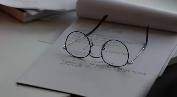 Okulary leżą na notatniku z planami. Czas na wymianę szkieł w okularach, by lepiej widzieć cele projektu.