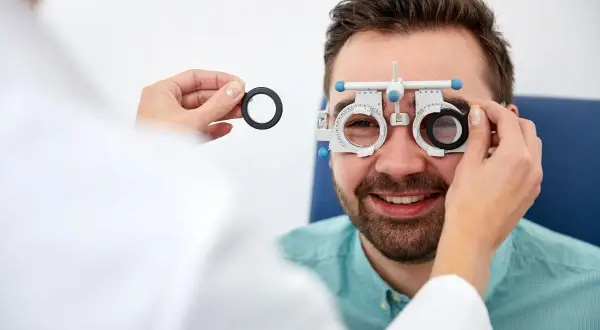 Optometrysta bada wzrok mężczyzny, który uśmiecha się, nosząc specjalne okulary.