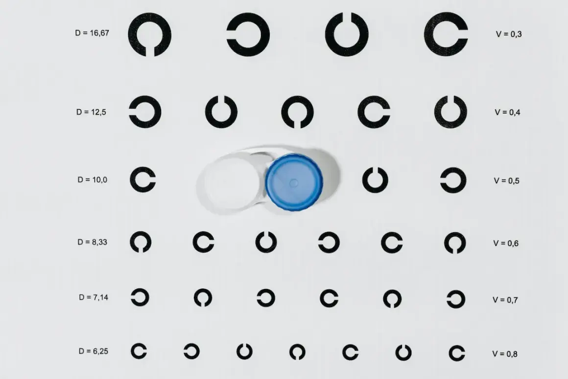 Na tablicy optometrycznej widać szereg symboli "C" oraz pojemnik na soczewki. Wartości D i V sugerują dobór soczewek, np. krzywizna soczewki 8,6 i 8,7.