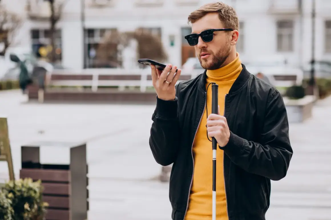 Mężczyzna w okularach, trzymający laskę i telefon, korzysta z technologii, która może być pomocna jak okulary dla niewidomych.