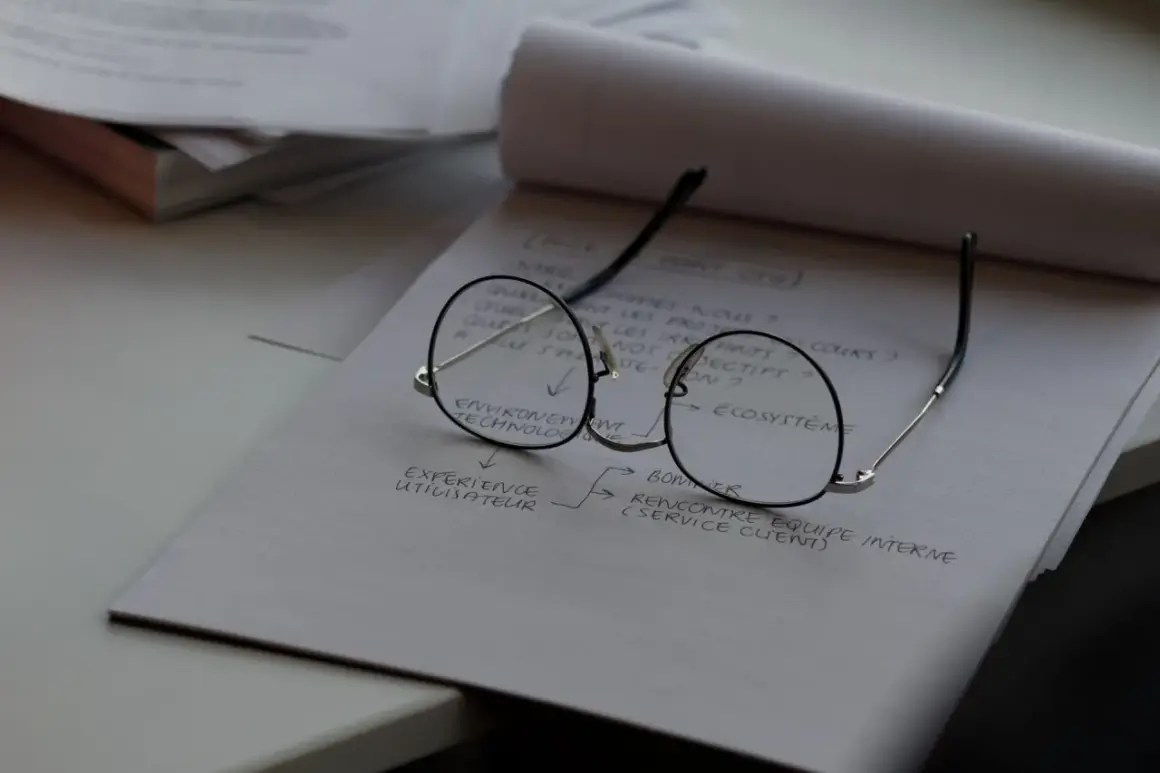 Okulary leżą na notatniku z planami. Czas na wymianę szkieł w okularach, by lepiej widzieć cele projektu.