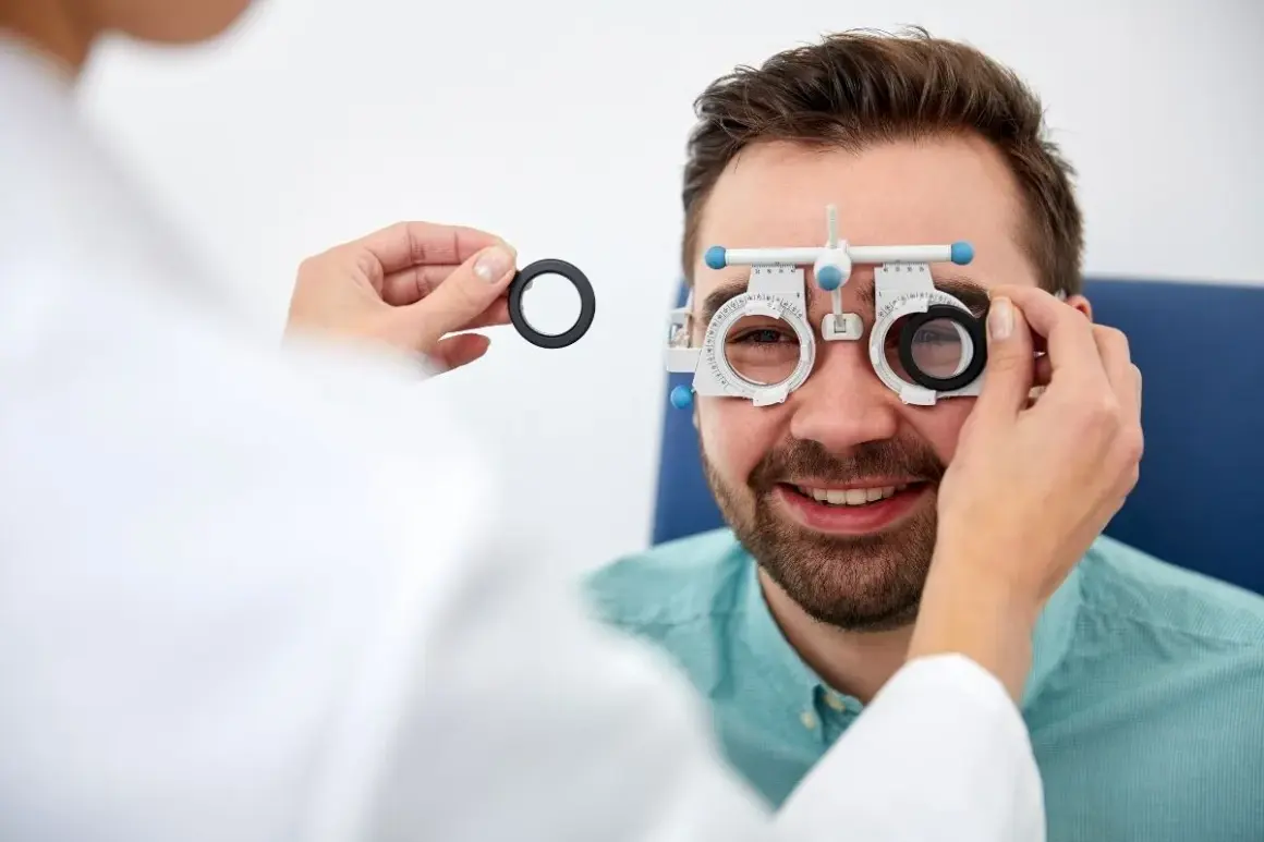 Optometrysta bada wzrok mężczyzny, który uśmiecha się, nosząc specjalne okulary.