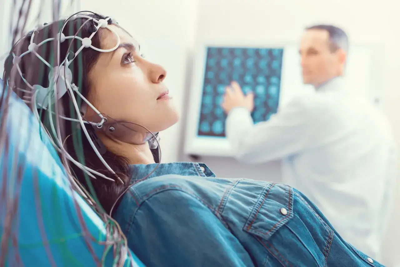 Kobieta w czepku z elektrodami przechodzi badanie EEG. Lekarz analizuje wyniki na ekranie.