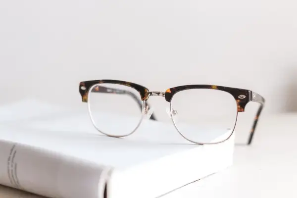 Okulary w stylu retro na białej książce. Nawet najmniejsza wada wzroku może wymagać takiego wsparcia.